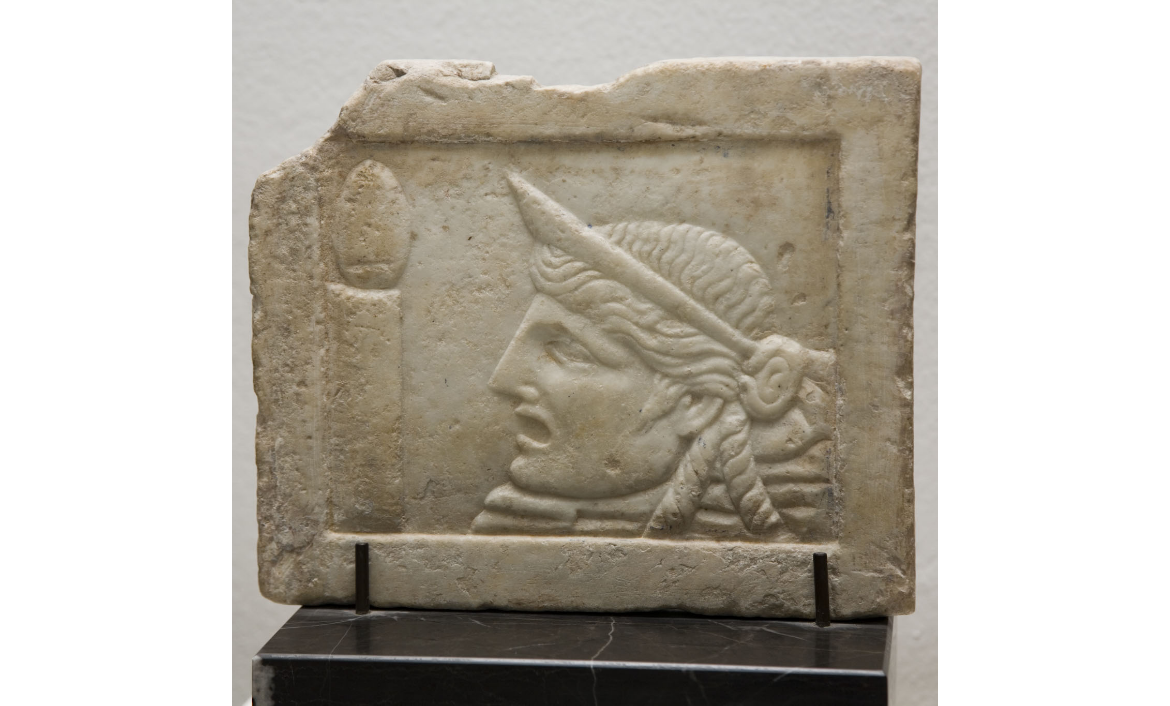[MR 3118] – Placa de marbre esculpida per les dues cares (pinax). A la cara ben conservada, una màscara teatral femenina davant d'un tympanum sobre columna. Procedeix de Tarragona. Segle II.